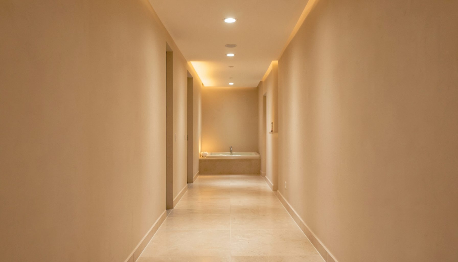 A serene spa corridor with soft beige walls, warm lighting, and a calm, restorative atmosphere